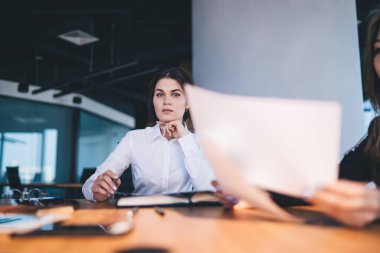 Modern ofiste masa başında oturup kameraya bakarken, beyaz bluzlu, ciddi ve zarif bir kadının konferansta belgeler üzerinde çalışması.