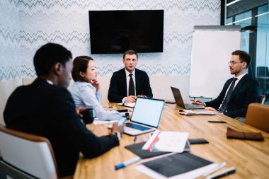 Konsantre ofis meslektaşları dikkatle dinliyorlar patron. Konferans odasındaki masada oturan aletleri kullanarak iş projesi hakkında konuşuyorlar. 