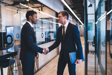 İş dünyasından çok ırklı erkek yöneticilerin yan görünüşü birbirlerine bakarken karşılıklı selamlaşmalar ve modern ofis salonunda el sıkışmalar.
