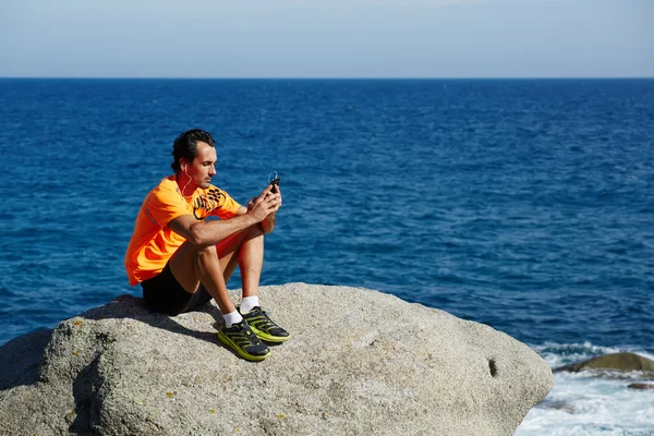 Мужчина бегун с помощью мобильного смартфона отдыхает после тренировки — стоковое фото