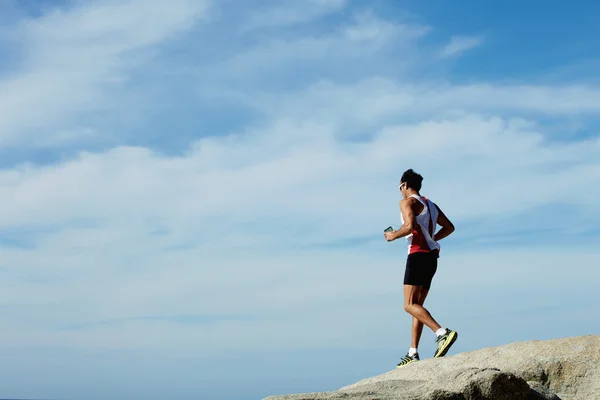 Νεαρός αθλητής τρέχει κάτω από πέρα από τους βράχους κατά συννεφιασμένο ουρανό — Φωτογραφία Αρχείου