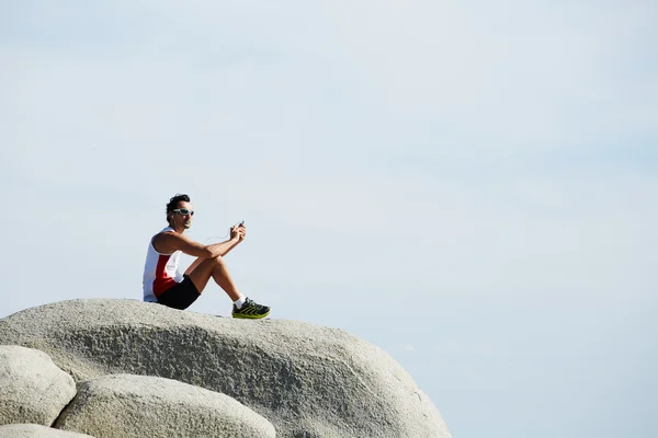 Člověk si přestávku a relaxovat, sedí na horské skále na obloze — Stock fotografie