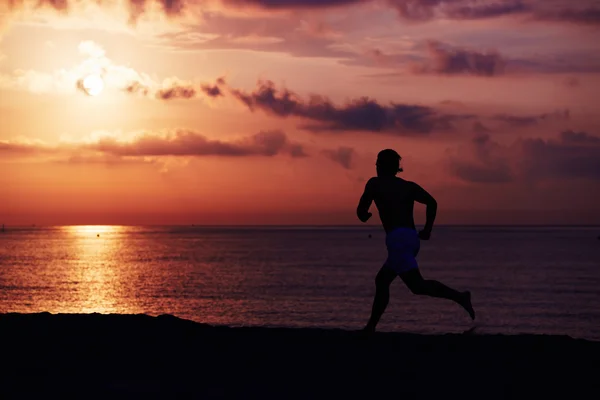 Silhouette di costruzione muscolare atleta correre veloce un tronco la spiaggia, corridore in azione jogging contro l'alba colorata sul mare, jogger maschile con corpo muscolare in azione — Foto Stock