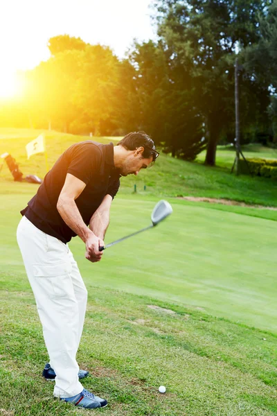 Jogador de golfe profissional em ação batendo bola de golfe ao pôr do sol — Fotografia de Stock