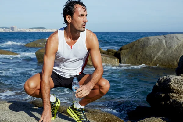 Mężczyzna pasuje runner odpoczynku siedząc na skałach na plaży — Zdjęcie stockowe