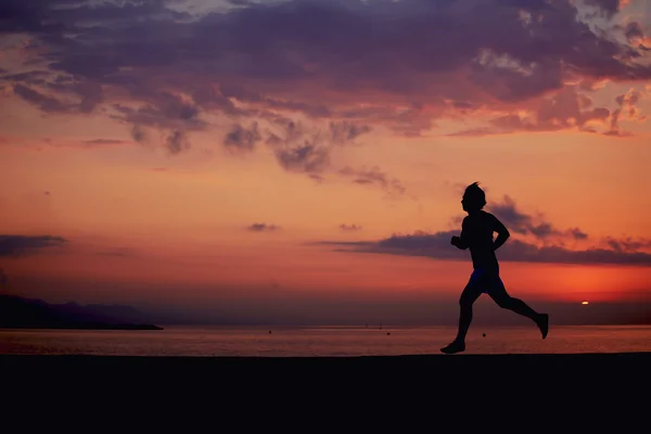 Sylwetka muskularnej budowy sportowca biegnie szybko dziennik plaży, biegacz w akcji jogging przed kolorowym wschodem słońca nad morzem, męski jogger z umięśnionym ciałem w akcji — Zdjęcie stockowe