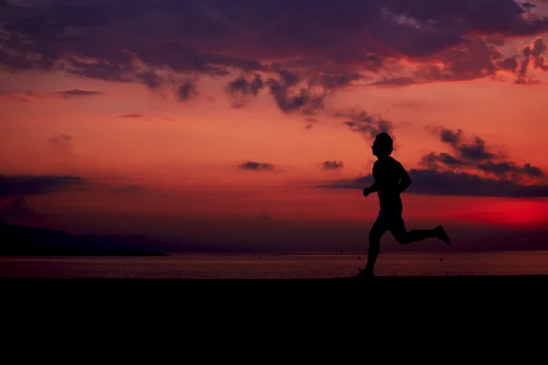 Perfetta e bella silhouette di uomo in forma sportiva che corre sulla spiaggia, allenamento di fitness mattutino all'aperto, giovane jogger che corre veloce all'alba colorata — Foto Stock