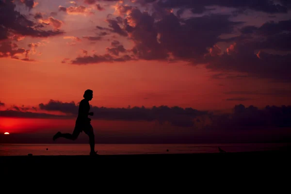 Perfekte und schöne Silhouette eines sportlich durchtrainierten Mannes, der am Strand läuft, morgendliches Fitnesstraining im Freien, junge Joggerin, die beim bunten Sonnenaufgang schnell läuft — Stockfoto