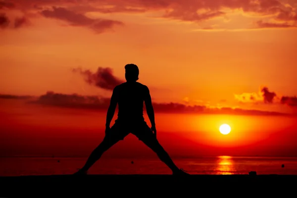 Силуэт спортсмена мужского пола, занимающегося кросс-тренировкой на красочном фоне восхода солнца, красивый силуэт спортсмена, делающего упражнения на растяжку стоя на пляже — стоковое фото