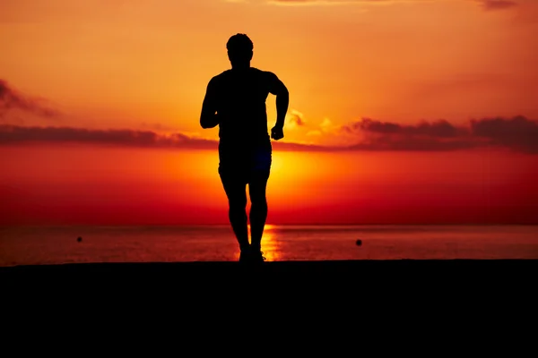 Silhueta de corredor atlético correndo na praia contra o nascer do sol laranja, corredor masculino com corpo muscular na corrida da manhã, corredor atraente em ação, fitness e conceito de estilo de vida saudável — Fotografia de Stock