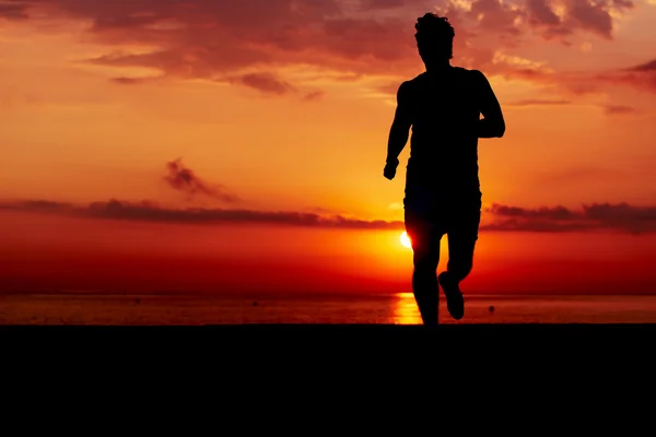 Silhuett av atletisk löpare jogging på stranden mot orange soluppgång, manliga löpare med muskulös kropp på morgon jog, attraktiva jogger i aktion, fitness och hälsosam livsstilskoncept — Stockfoto