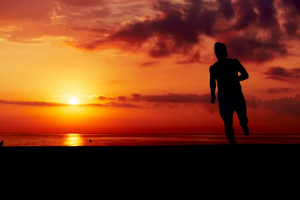 Silhueta de corredor masculino em ação, corredor atraente no treinamento matinal na praia, homem correndo para pôr do sol colorido na praia, fitness e conceito de estilo de vida saudável — Fotografia de Stock