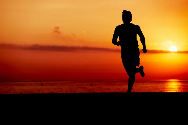 男性的赛跑者在行动、 有吸引力慢跑者在早晨在沙滩上，培训人跑进多彩日落海滩、 健身和健康的生活方式概念的剪影 — 图库照片