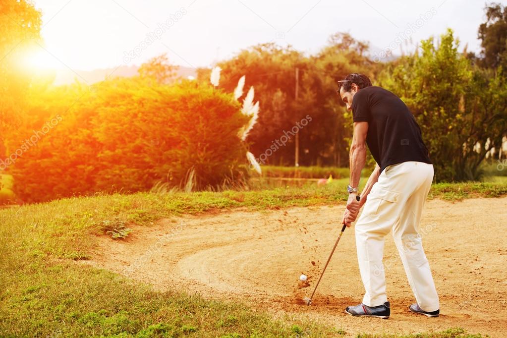 Man hitting golf ball from sand trap at sunny evening