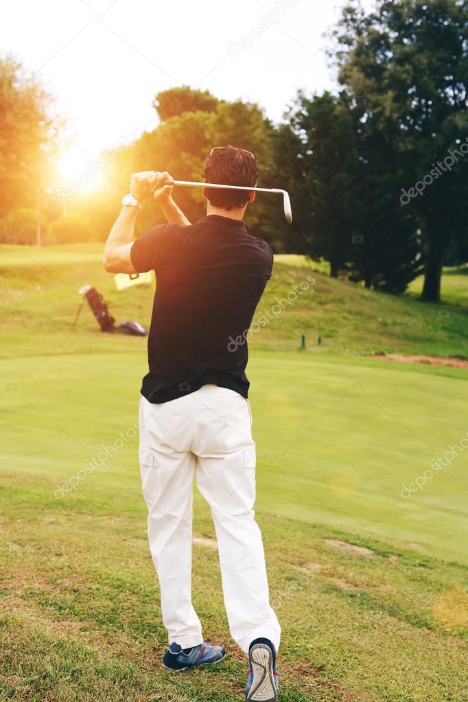 Golfer swinging his driver and looking away playing at sunset