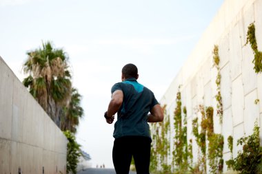 Back view portrait of dark skinner male runner jogging with high speed at sunny afternoon outdoors