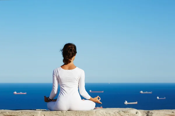 Young woman practices yoga on high altitude with sea ships view on background — Stockfoto