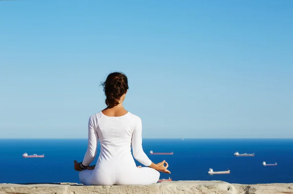 Young woman practices yoga on high altitude with sea ships view on background — Stok fotoğraf