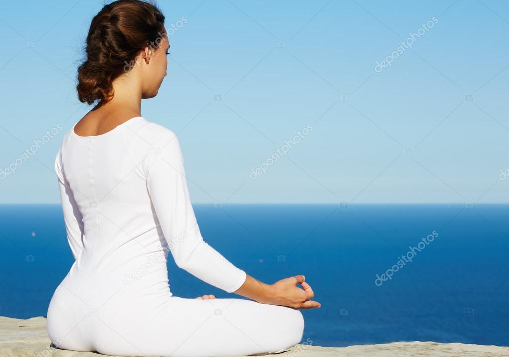 Young brunette woman makes yoga meditation at sunny evening outdoors with beautiful view of sea on background