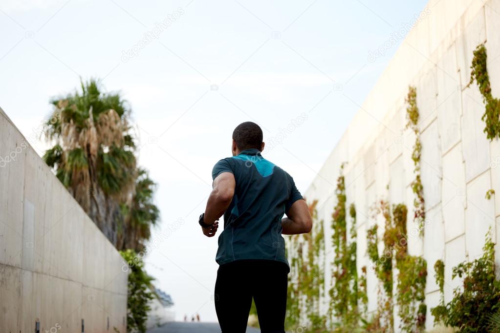 Back view portrait of dark skinner male runner jogging with high speed at sunny afternoon outdoors
