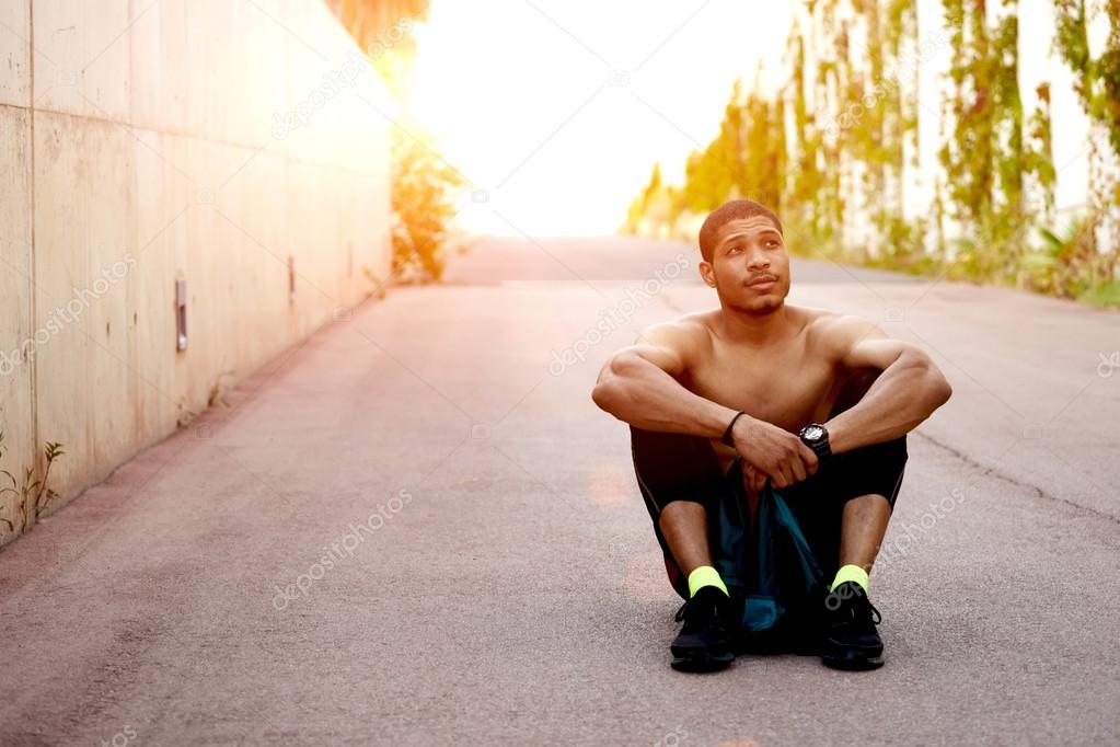 Healthy young african american runner having a rest after workout while sitting on the ground outdoors