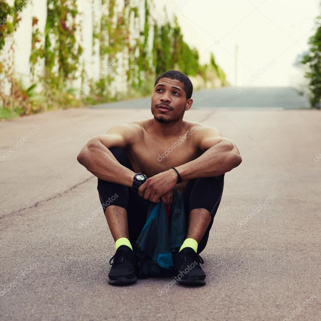 Athletic male runner resting after training outdoors while sitting on the ground