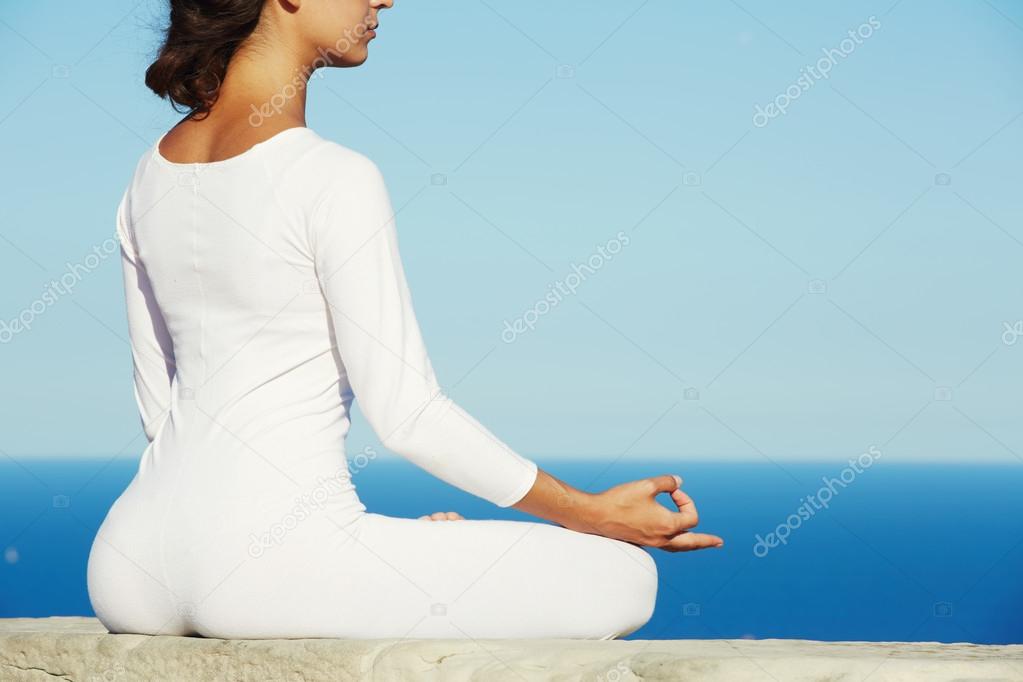 Brunette woman makes yoga meditation on high altitude with blue sea on background at sunny evening
