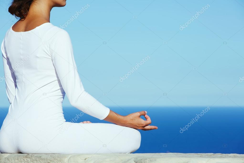 Cropped image portrait of young attractive female makes yoga on ocean background at sunny day