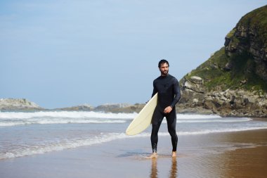 Sörf tahtasına onun surfboard ile arka plan, okyanusta taşıyan yakışıklı sörfçü yürüyüşler Sahilde yürüyüş tutarak çekici profesyonel sörfçü görüntü filtre