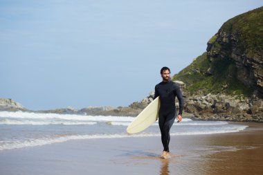 Sörf tahtasına onun surfboard ile arka plan, okyanusta taşıyan yakışıklı sörfçü yürüyüşler Sahilde yürüyüş tutarak çekici profesyonel sörfçü görüntü filtre