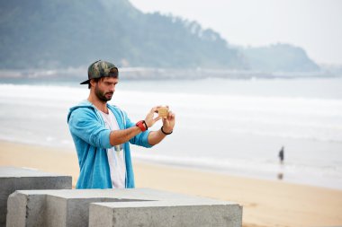 Young attractive hipster man taking a picture of beautiful beach view with mobile telephone