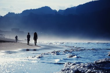 Silhouette young couple walking on the beach at evening with amazing mountains around bay