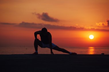 Silhouette of athletic build runner stretching the legs outdoors, runner prepare for workout