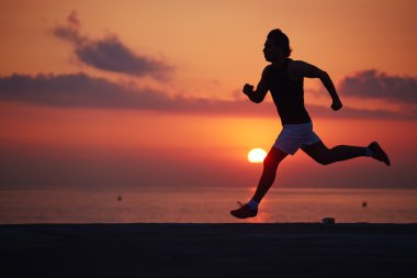 Silhouette of muscular build runner jogging on the beach at amazing orange sunrise