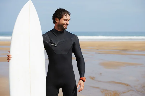 Portré a csípő fehér szörfdeszka állva az óceán, a strand, a férfi profi szörfös srác öltözött ruha kész szörfözés a nagyok a hullámok, boldog szörfös tartja a fedélzeten, napsütéses nyári napon — Stock Fotó