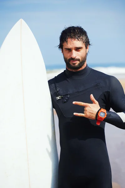 Portrait of hipster guy with white surfboard standing on ocean the beach, professional surfer man dressed in wetsuit ready to surfing on big waves, happy surfer holding his board at sunny summer day — Stock Photo, Image