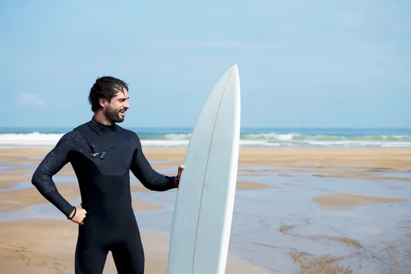 Atractivo joven surfista sosteniendo tabla de surf mientras está de pie en la playa mirando al océano para encontrar el lugar perfecto para ir olas de surf, surfista profesional con tabla de surf mirando al océano, imagen filtrada — Foto de Stock