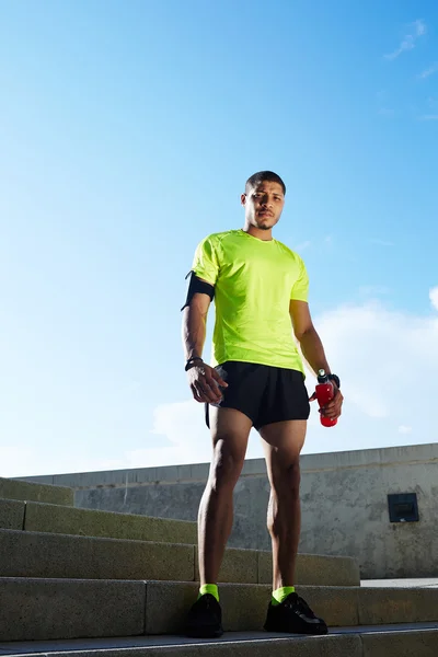 Молодой темнокожий бегун с мускулистой стойкой против мягкого солнечного света на открытом воздухе, красивый здоровый мужчина в яркой флуоресцентной спортивной одежде, спортивная концепция фитнеса — стоковое фото
