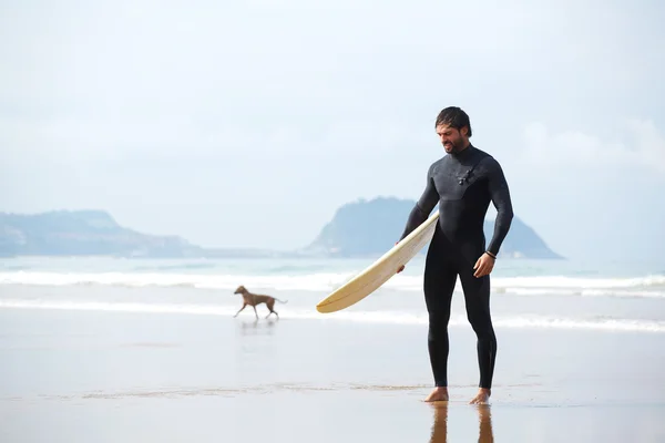 Atractivo joven surfista sosteniendo tabla de surf mientras está de pie en la playa mirando al océano para encontrar el lugar perfecto para ir olas de surf, surfista profesional con tabla de surf mirando al océano, imagen filtrada —  Fotos de Stock