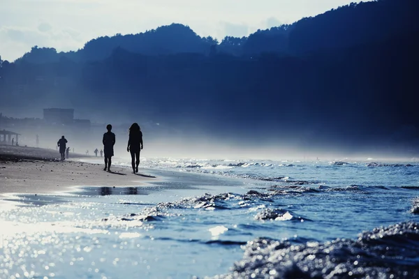 Silueta joven pareja caminando en la playa por la noche con increíbles montañas alrededor de la bahía — Foto de Stock