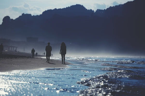 En la fría noche la gente caminando en la playa tocando las olas del océano — Foto de Stock