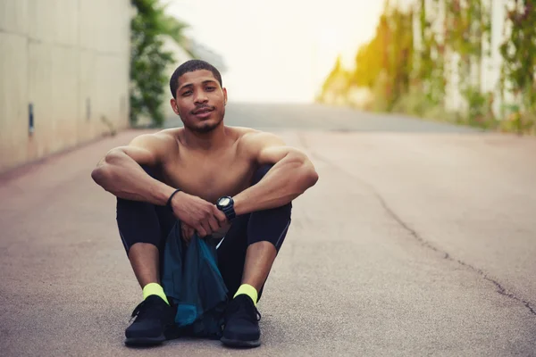 Portrait of handsome fit man with muscular body sitting on the road and resting after run — ストック写真