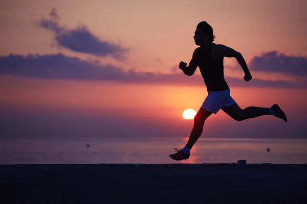 Athletic build jogger running with high speed along the beach at colorful sunrise — Stock fotografie