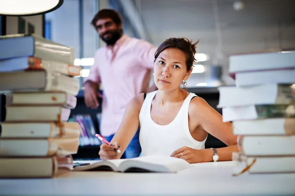 Frustrated college student sitting at the desk with huge pile of study book in university library — Zdjęcie stockowe