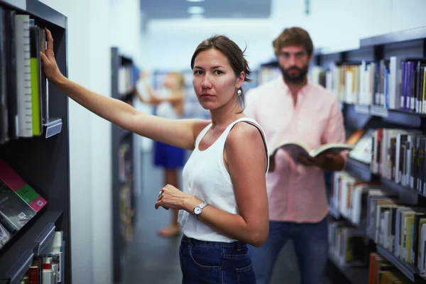 Zwei internationale Studenten auf der Suche nach Büchern in der Bibliothek während der Aufnahmeprüfungen — Stockfoto
