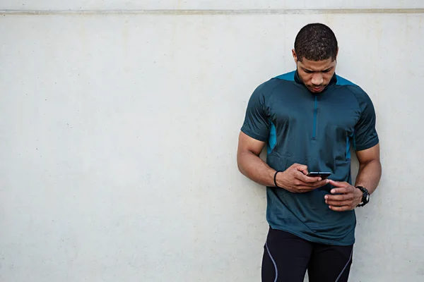 Hombre en forma descansando después del entrenamiento al aire libre sosteniendo el teléfono inteligente móvil — Foto de Stock