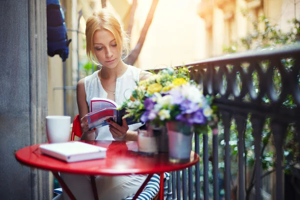 Jonge vrouw met een kopje koffie op home balkon lezen van het boek — Stockfoto