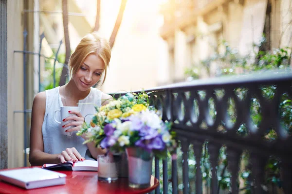 Bella giovane donna lettura libro mentre sedersi sul suo balcone di casa — Foto Stock