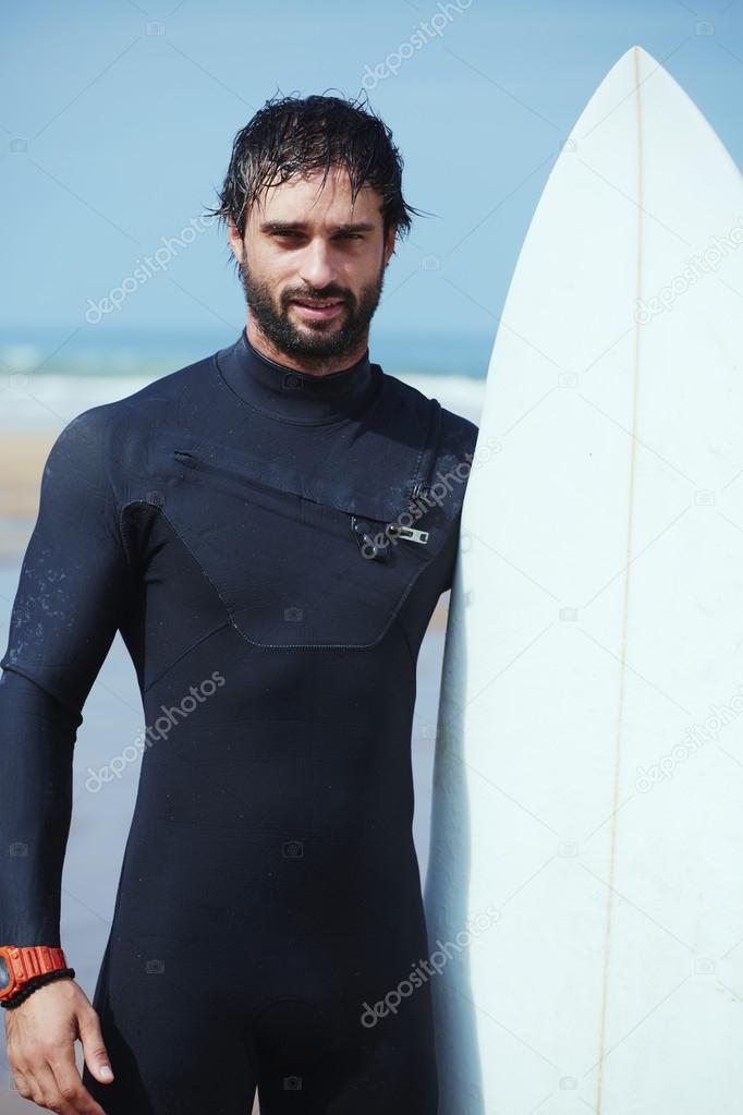 Portrait of hipster guy with white surfboard standing on ocean the beach, professional surfer man dressed in wetsuit ready to surfing on big waves, happy surfer holding his board at sunny summer day