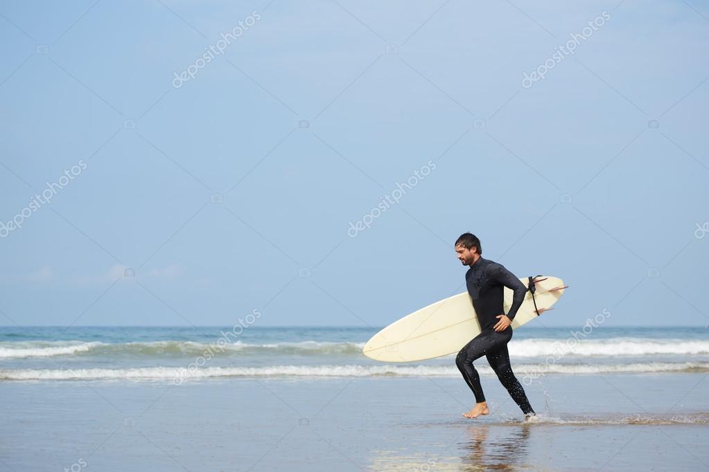 Joven surfista atractivo corre con tabla de surf a lo largo de la
